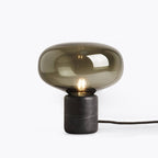 A closer studio crop of the Clérachic table lamp on white, the smoke-grey dome and filament bulb centred in frame.