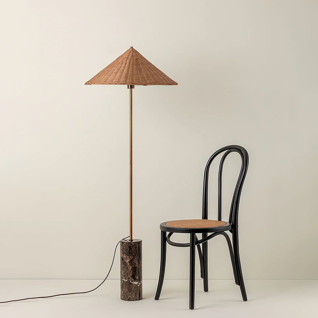 Standing full length next to a black bentwood cane chair, a Clérachic rattan cone-shade floor lamp rests on its marble base.