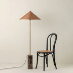 Standing full length next to a black bentwood cane chair, a Clérachic rattan cone-shade floor lamp rests on its marble base.