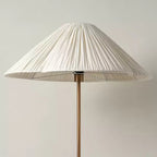 Close-up of the pleated white shade and brass stem on a Clérachic floor lamp, with its bottle-shaped base visible below.