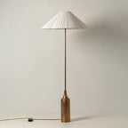 The cord and inline switch rest on the floor beside this Clérachic pleated white cone-shade floor lamp's brass bottle base.