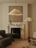 Clérachic pleated white pendant and floor lamp with a brass bottle base glow beside a marble fireplace and dark sofa.