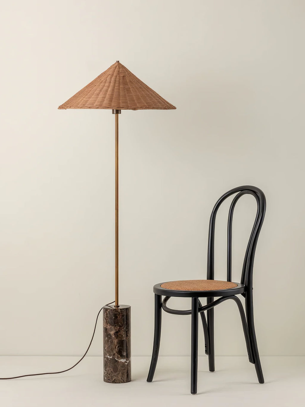 Clérachic rattan cone-shade floor lamp on a marble cylinder base standing beside a black bentwood chair with a woven cane seat.