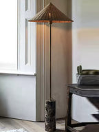 Clérachic rattan cone-shade floor lamp beside a small round table, with its dark marble base and brass stem in daylight.