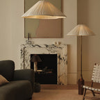 Clérachic pleated white shade pendant and matching floor lamp glow beside a marble fireplace and dark green sofa in a living room.