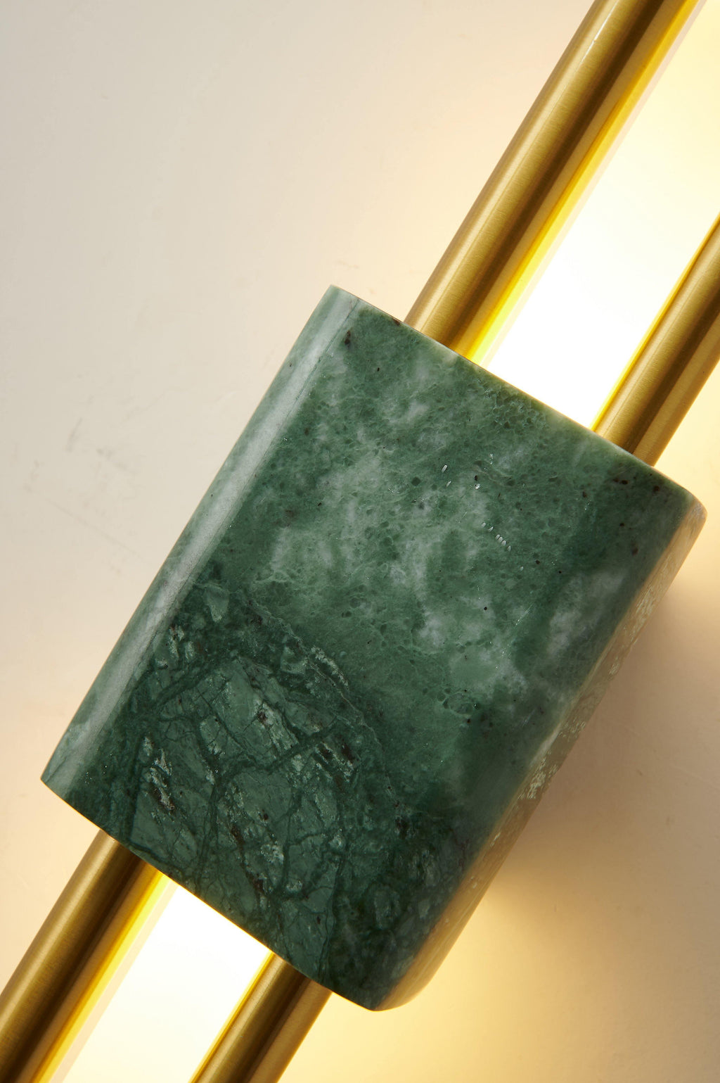 Extreme close-up of the green marble texture and brass rod on this Clérachic wall light, its opal tube glowing.