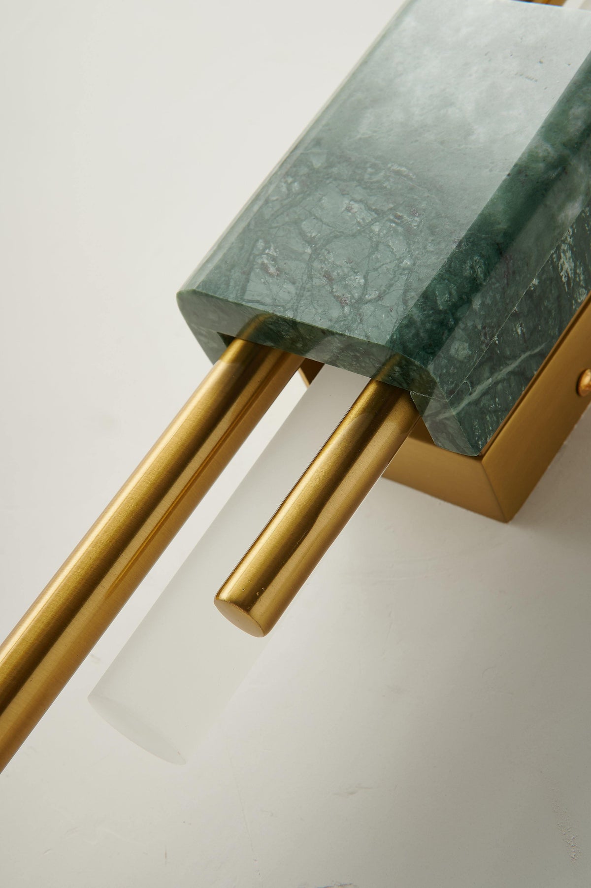 Macro detail of the marble corner and brass rods on this Clérachic wall sconce, unlit, against a white backdrop.