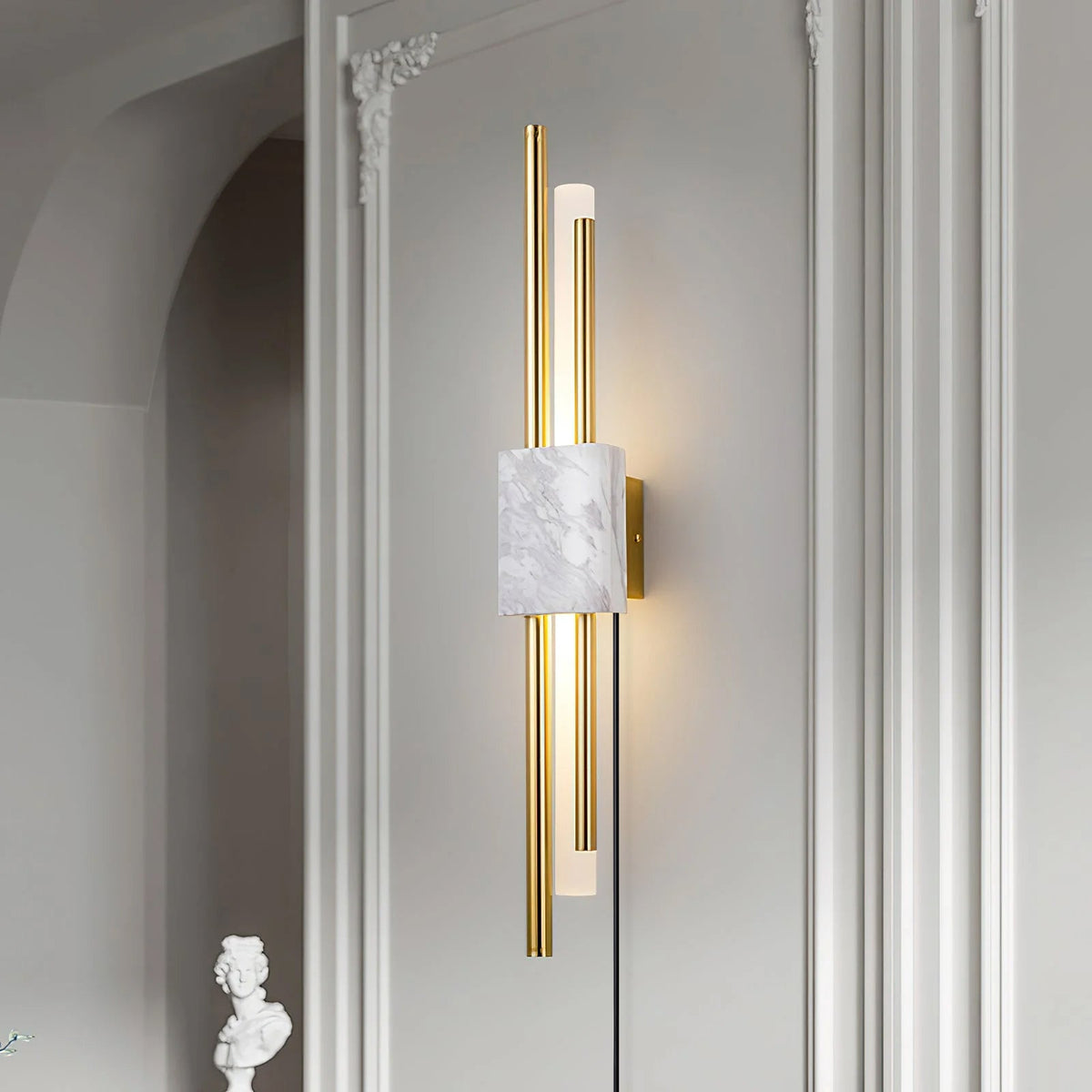 A white marble block anchors this Clérachic wall light, mounted in a plastered archway beside a column and a small bust.