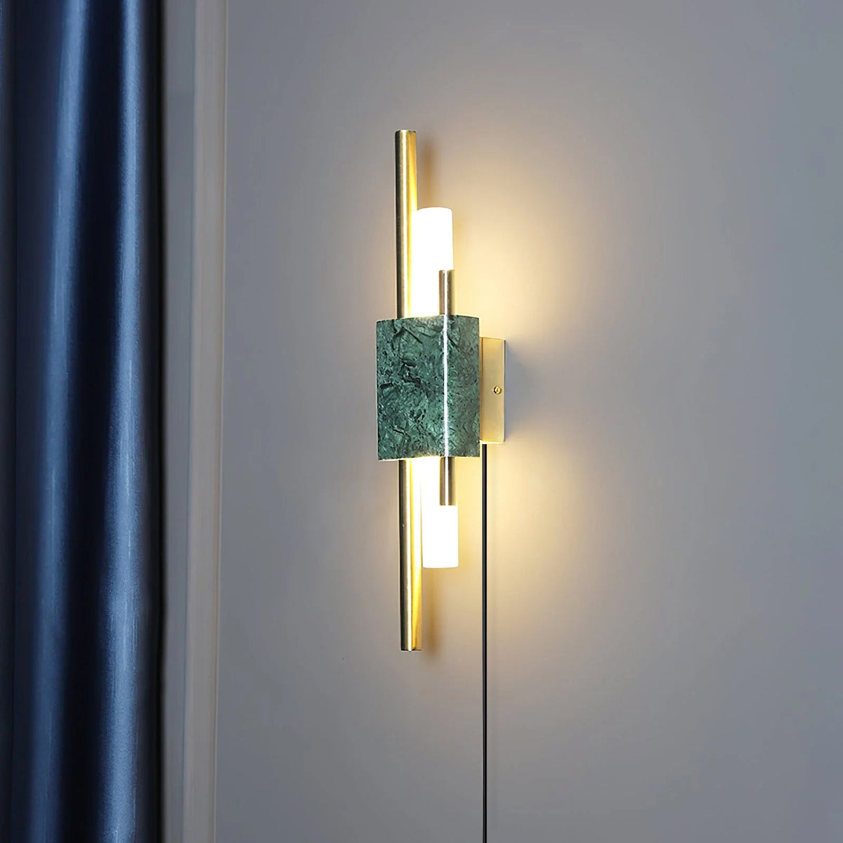 This Clérachic wall sconce glows warm against a deep navy curtain, its green marble block catching light beside slim brass rods.