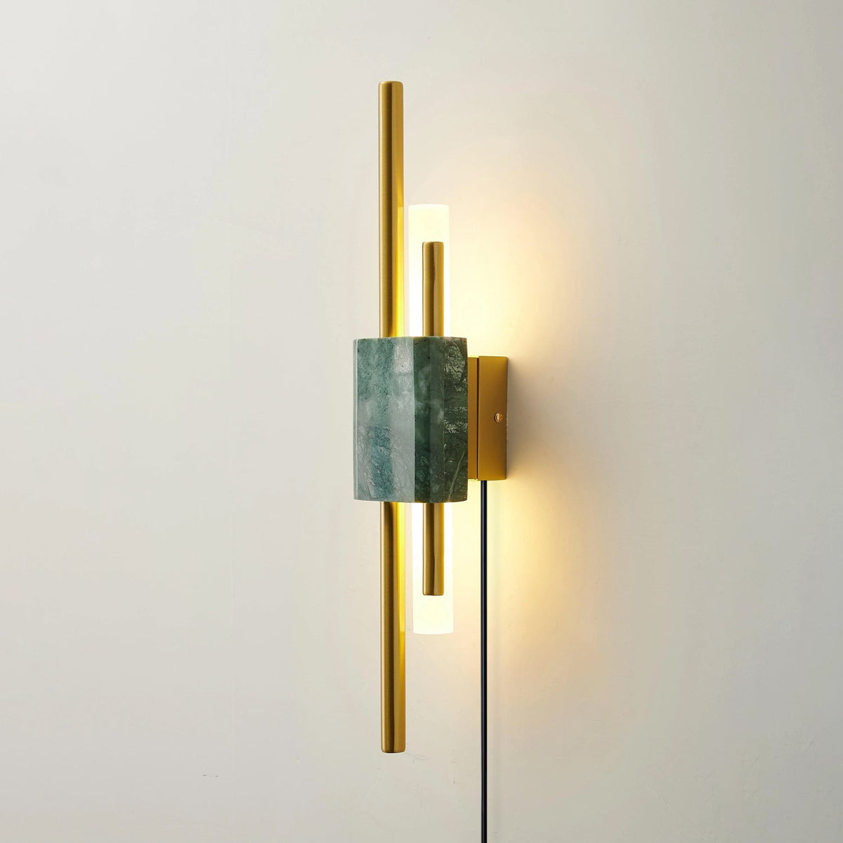 Close crop of the Clérachic wall sconce on an off-white wall, its green marble block sitting between two brass light rods.