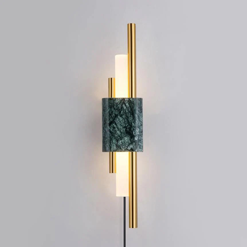 Mounted on a plain wall with its cord hanging visible, this Clérachic wall sconce shows a green marble block between brass rods.