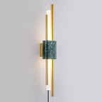 A green marble block sits between glowing brass rods on this Clérachic wall sconce, photographed straight-on against a grey wall.