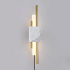 With its plug-in cord visible below, this Clérachic wall sconce's brass rods and frosted glass tubes glow against a grey wall.