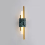 Vertical brass rods flank a green marble block on this Clérachic wall sconce, its frosted glass tubes lit against a plain grey wall.