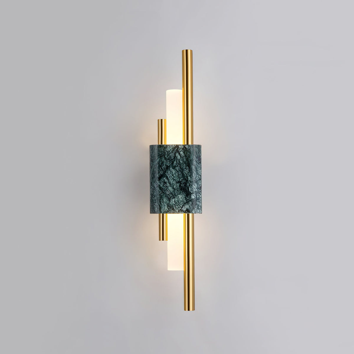 Vertical brass rods flank a green marble block on this Clérachic wall sconce, its frosted glass tubes lit against a plain grey wall.