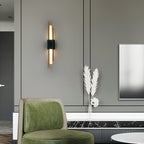 Mounted beside a green armchair and a small side table, this Clérachic wall sconce's brass rods glow softly in a living room.