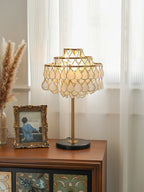Clérachic table lamp lit on a dark wood sideboard, framed beside a gilt vintage photograph near a window.