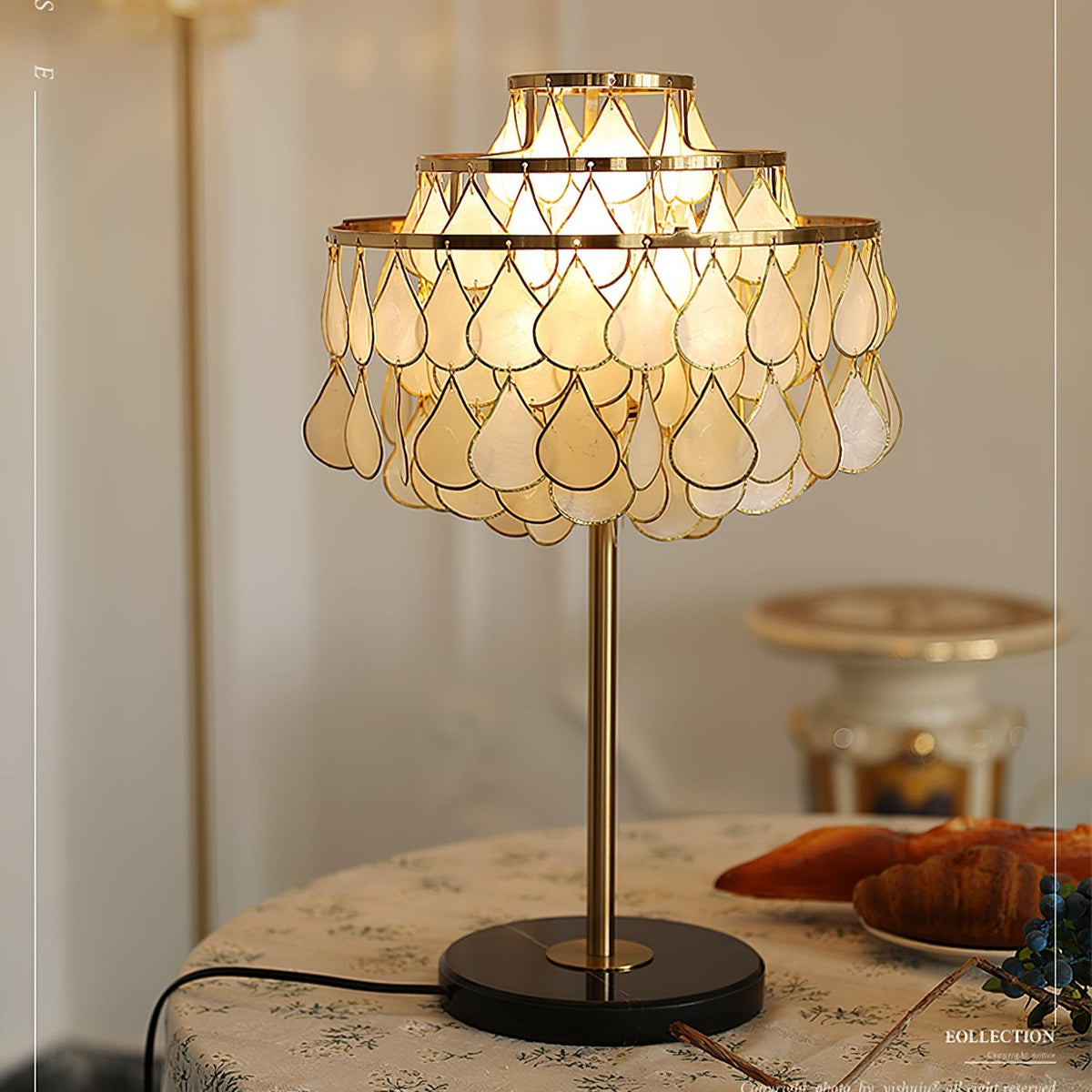 A porcelain angel figurine, vase of flowers and book share the round table where the Clérachic table lamp glows.