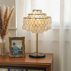 Clérachic table lamp lit on a dark wood sideboard beside dried pampas grass and a gilt-framed vintage photograph.