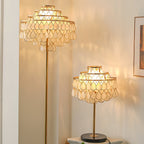 Clérachic table lamp and its taller floor-lamp companion glowing in a room with tall sheer-curtained windows.