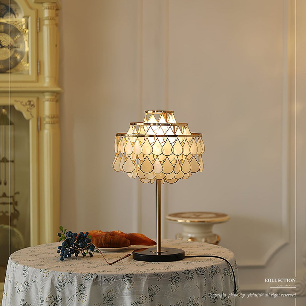 A stone urn blurs in the background as the Clérachic table lamp glows on a floral-cloth table with croissants and blueberries.