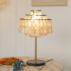 Clérachic teardrop shell table lamp glowing on a round table set with a china plate of croissants and blueberries.