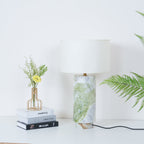 Clérachic table lamp styled with the same books and flower vase, fern fronds framing the shot from the right.