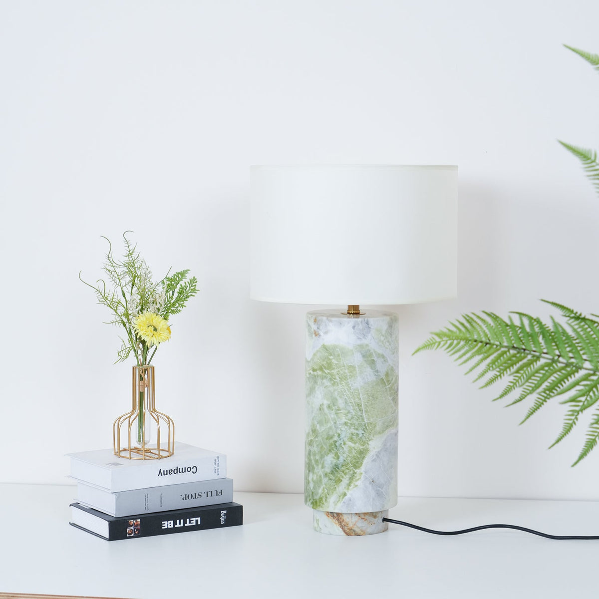 Clérachic table lamp styled with the same books and flower vase, fern fronds framing the shot from the right.