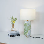 Clérachic table lamp close beside the flower-topped books, its green marble base and white drum shade centred in frame.