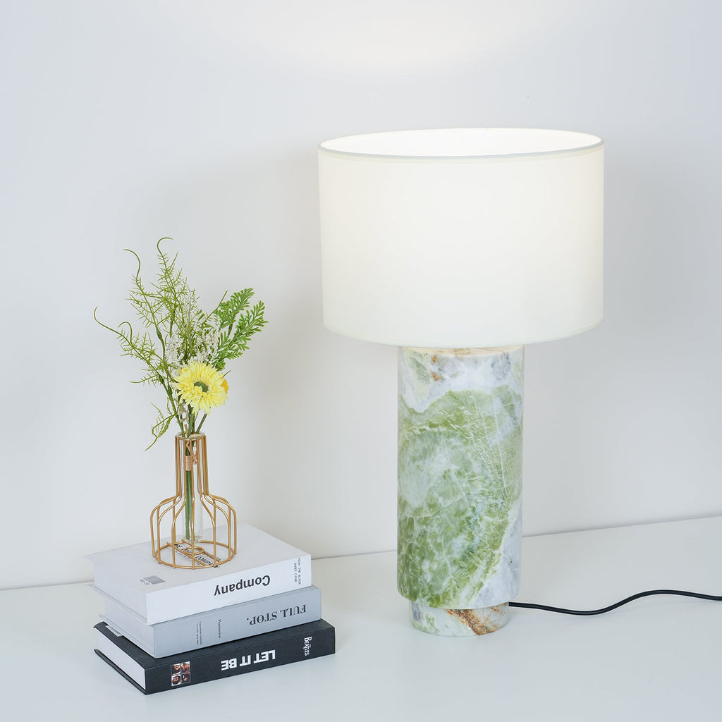 Clérachic table lamp beside a stack of books topped with a small vase of yellow flowers, on a plain white surface.