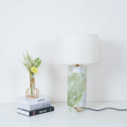Clérachic table lamp beside the book stack and vase, with fern fronds now visible in the lower corner of the shot.