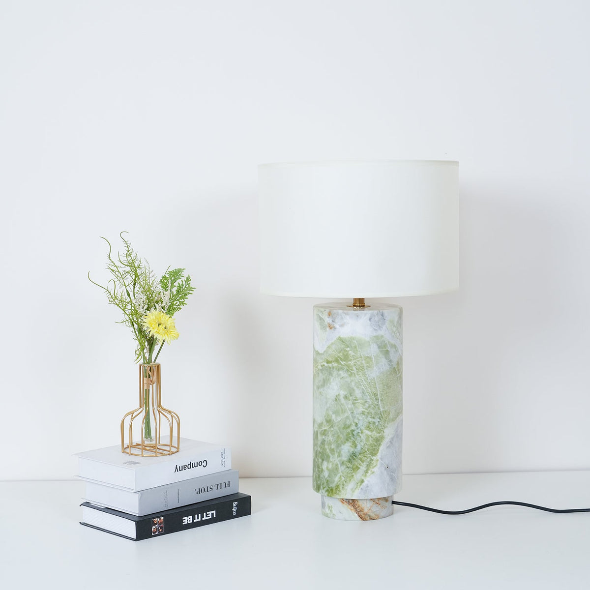 Clérachic table lamp beside the book stack and vase, with fern fronds now visible in the lower corner of the shot.