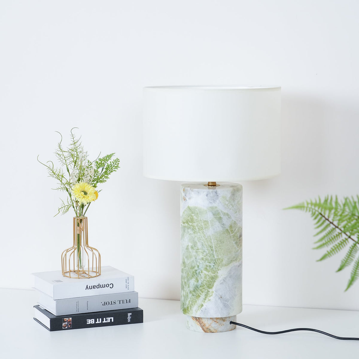 Clérachic table lamp in a wider crop, showing the full drum shade above the green marble base and fern fronds nearby.