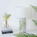 Clérachic table lamp framed closely by fern fronds on both sides, with the flower vase and books to its left.