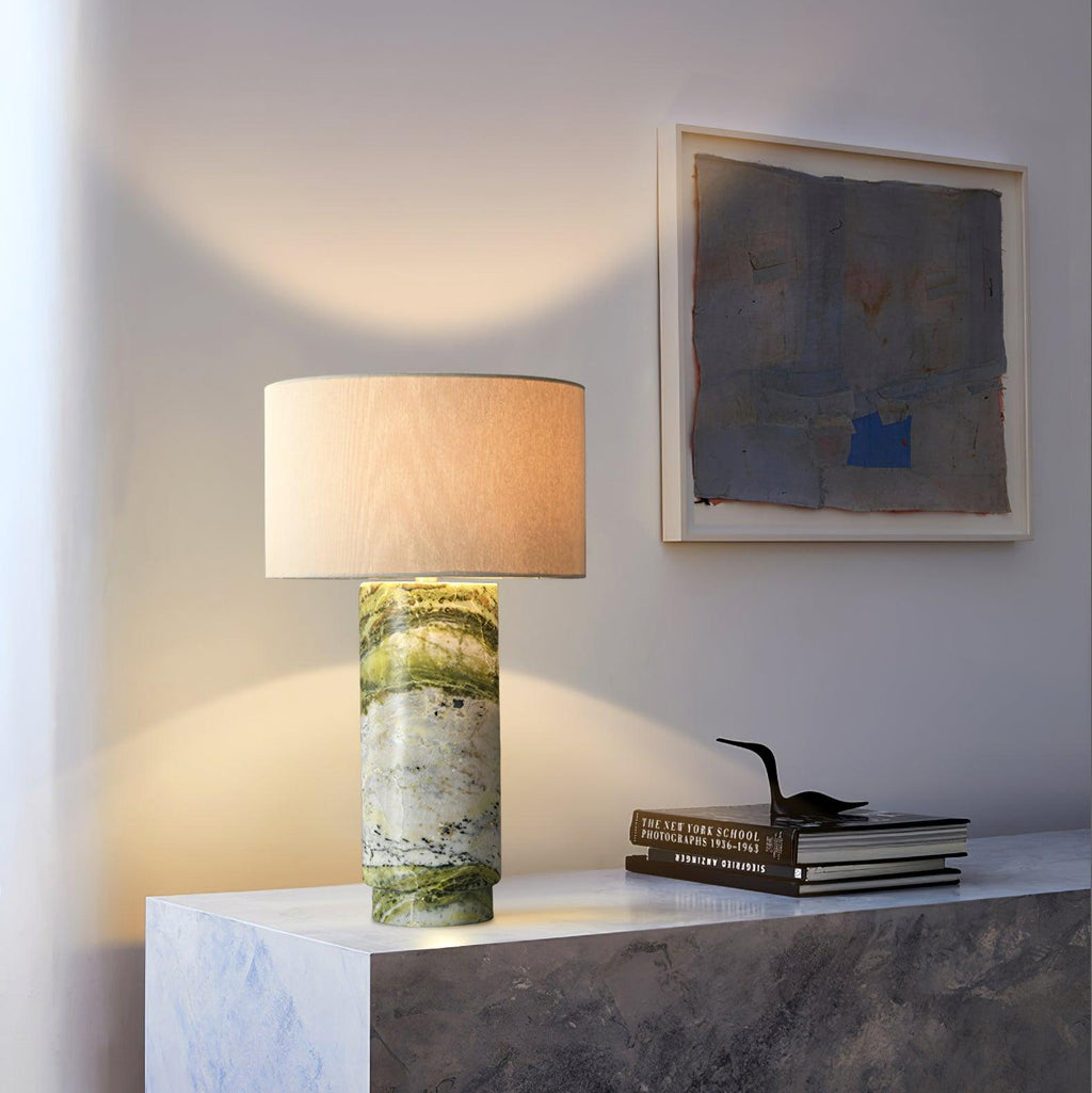 Clérachic table lamp lit on a two-tone marble plinth, beside a framed abstract artwork and a stack of photography books.