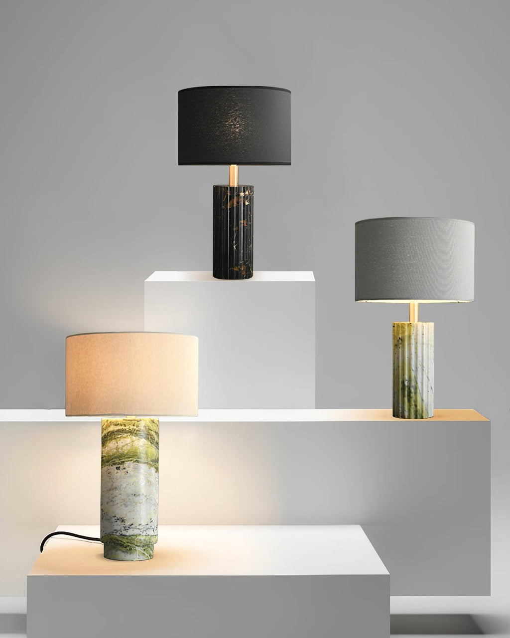 Clérachic table lamp displayed alongside two other finish options on staged plinths, its own base lit at the front.