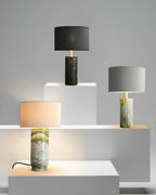 Clérachic table lamp displayed alongside two other finish options on staged plinths, its own base lit at the front.