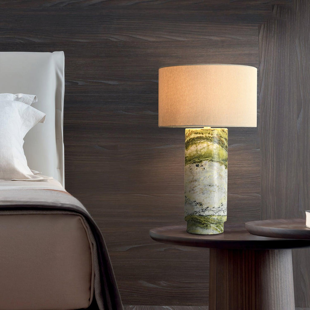Clérachic table lamp lit on a dark wood nightstand beside a bed with white linen, set against a dark panelled wall.