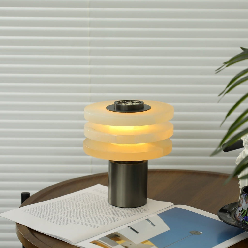 The lit alabaster lamp framed against white blinds and green palm leaves, giving off a soft amber band