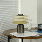 The unlit alabaster lamp on a round walnut side table beside an open magazine and a white angel figurine