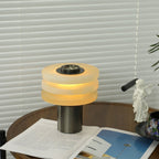 Room view of the lit alabaster lamp on the walnut side table, compact next to a teacup and magazine