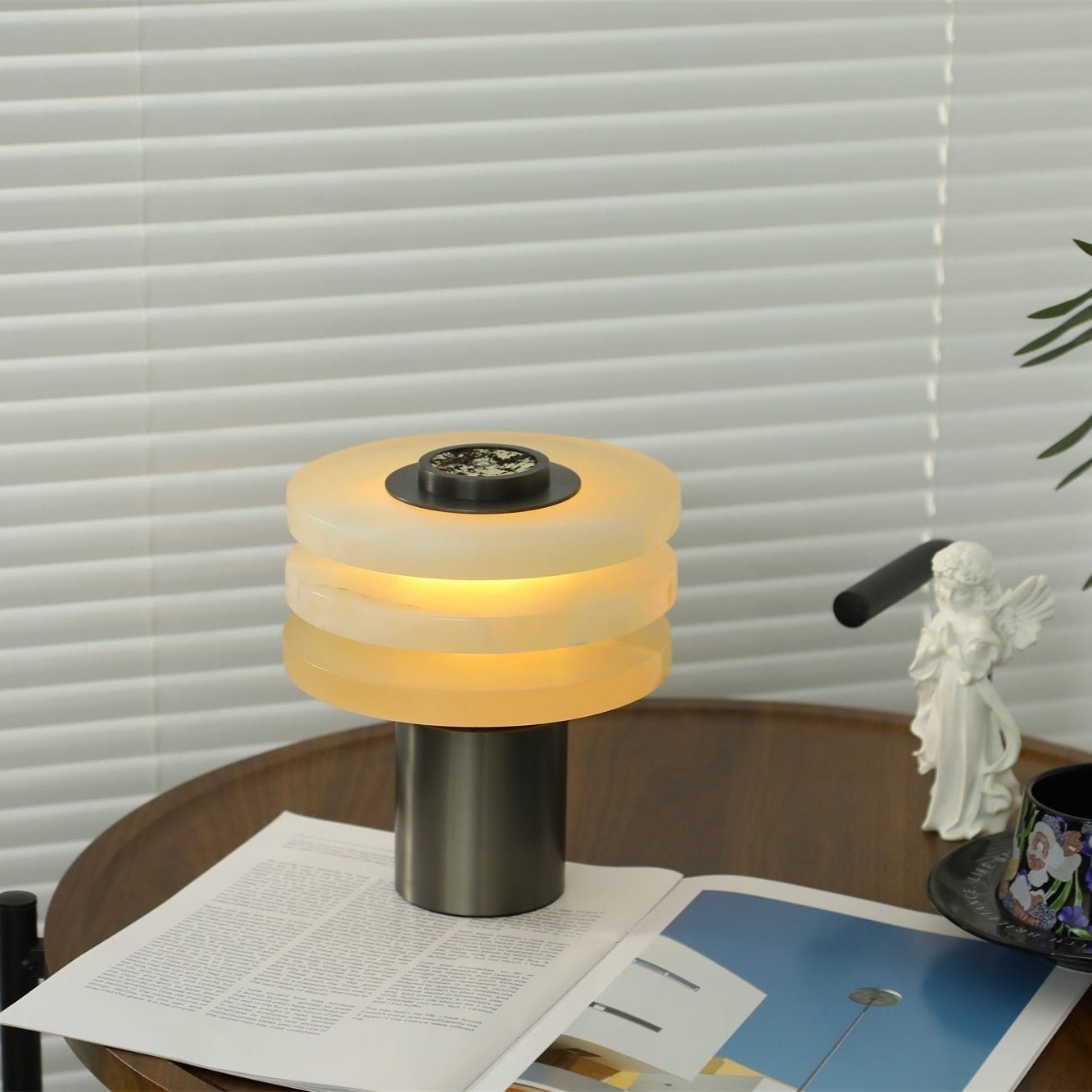 Room view of the lit alabaster lamp on the walnut side table, compact next to a teacup and magazine
