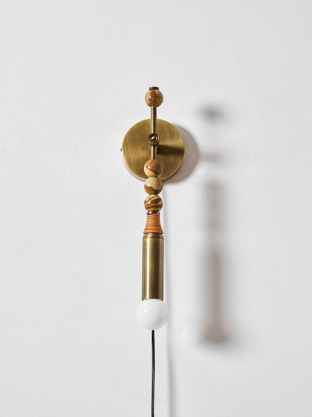Clérachic wall light on a plain white wall, wood beads above a lit globe, its soft shadow cast to one side.