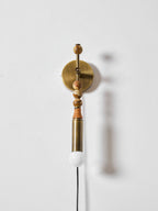 Clérachic wall light on a plain white wall, wood beads above a lit globe, its soft shadow cast to one side.