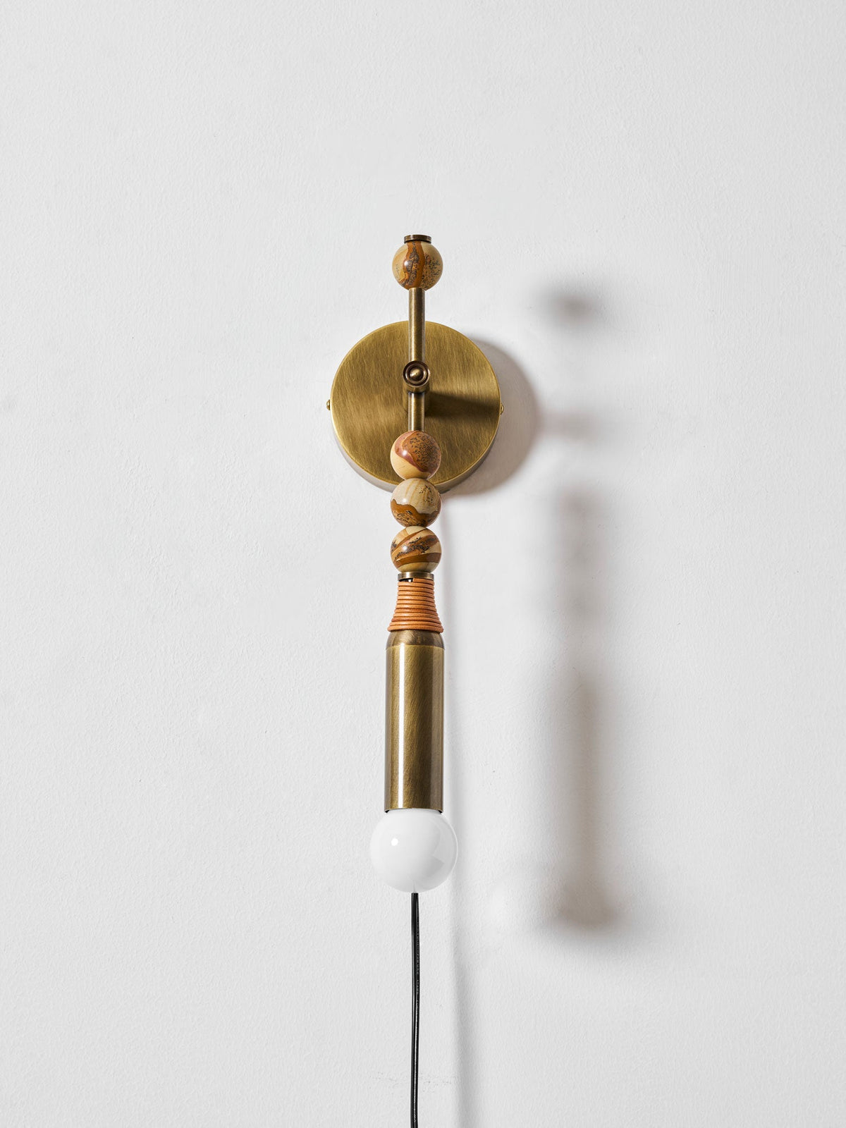 Clérachic wall light on a plain white wall, wood beads above a lit globe, its soft shadow cast to one side.
