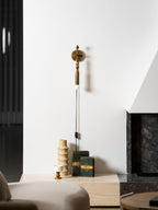 Clérachic plug-in wall lamp above a lounge side table with books and a ceramic vase, dark beads and a lit globe.
