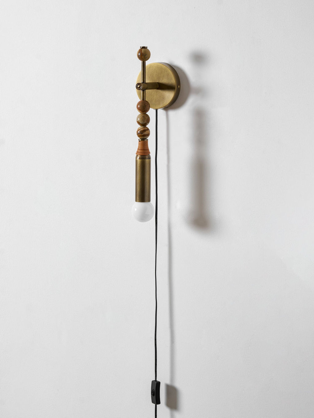 Clérachic wall sconce on a plain white wall, mixed bead shapes above a lit glass globe and hanging cord.