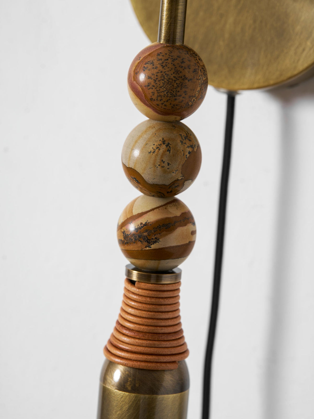 Close-up of three amber, tortoiseshell-patterned stone beads on a Clérachic wall lamp above a leather-wrapped tube.