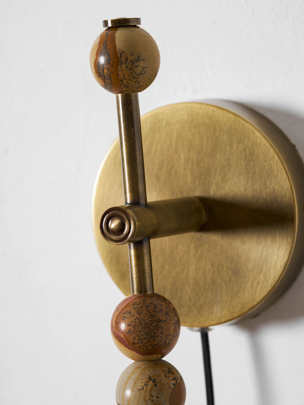 Close-up of a Clérachic wall sconce's painted brass finial ball and mounting joint, a wood bead just below.