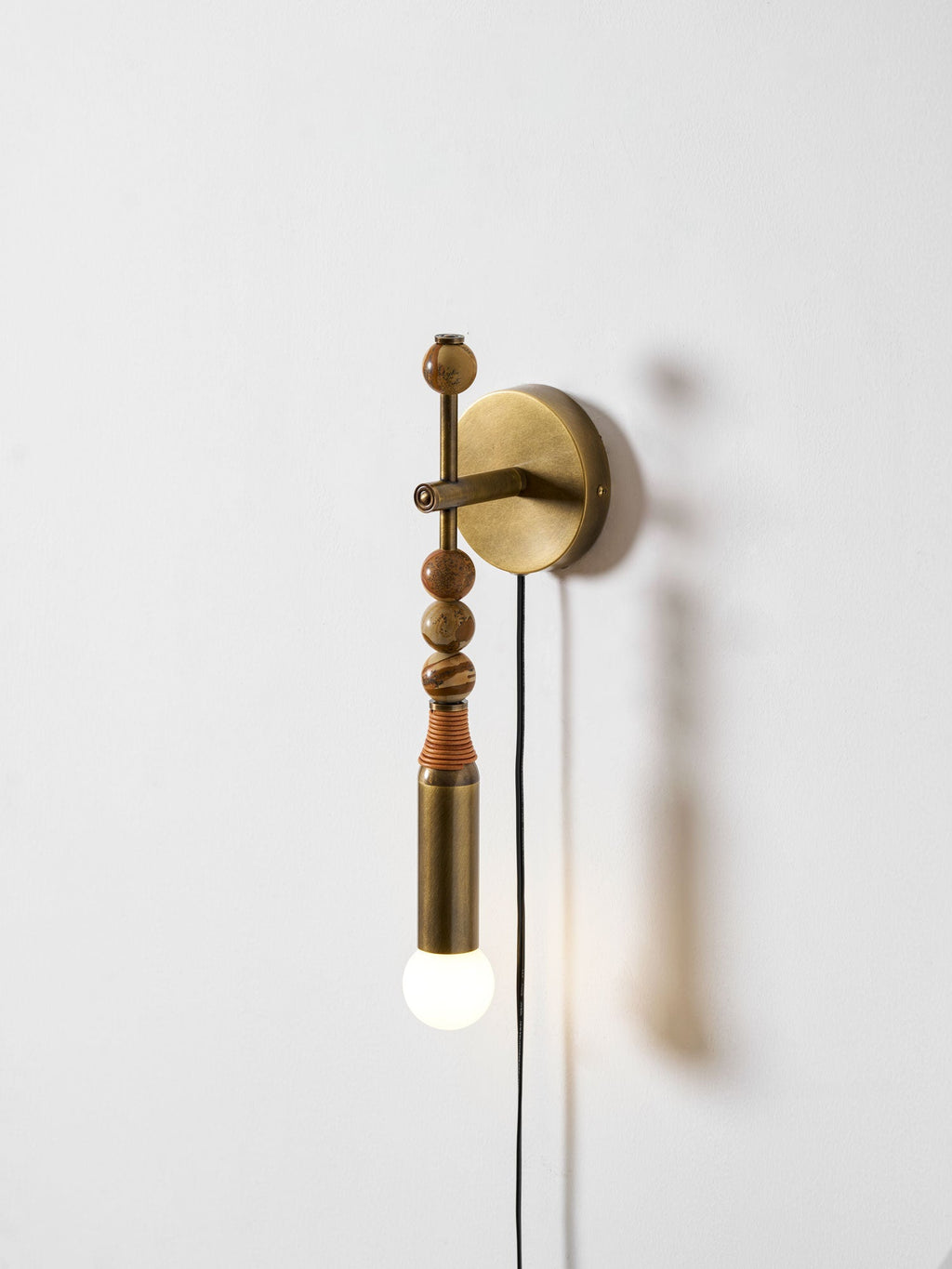 Clérachic plug-in wall lamp on a plain wall, wood beads above a lit glass globe, cord looping down to its plug.